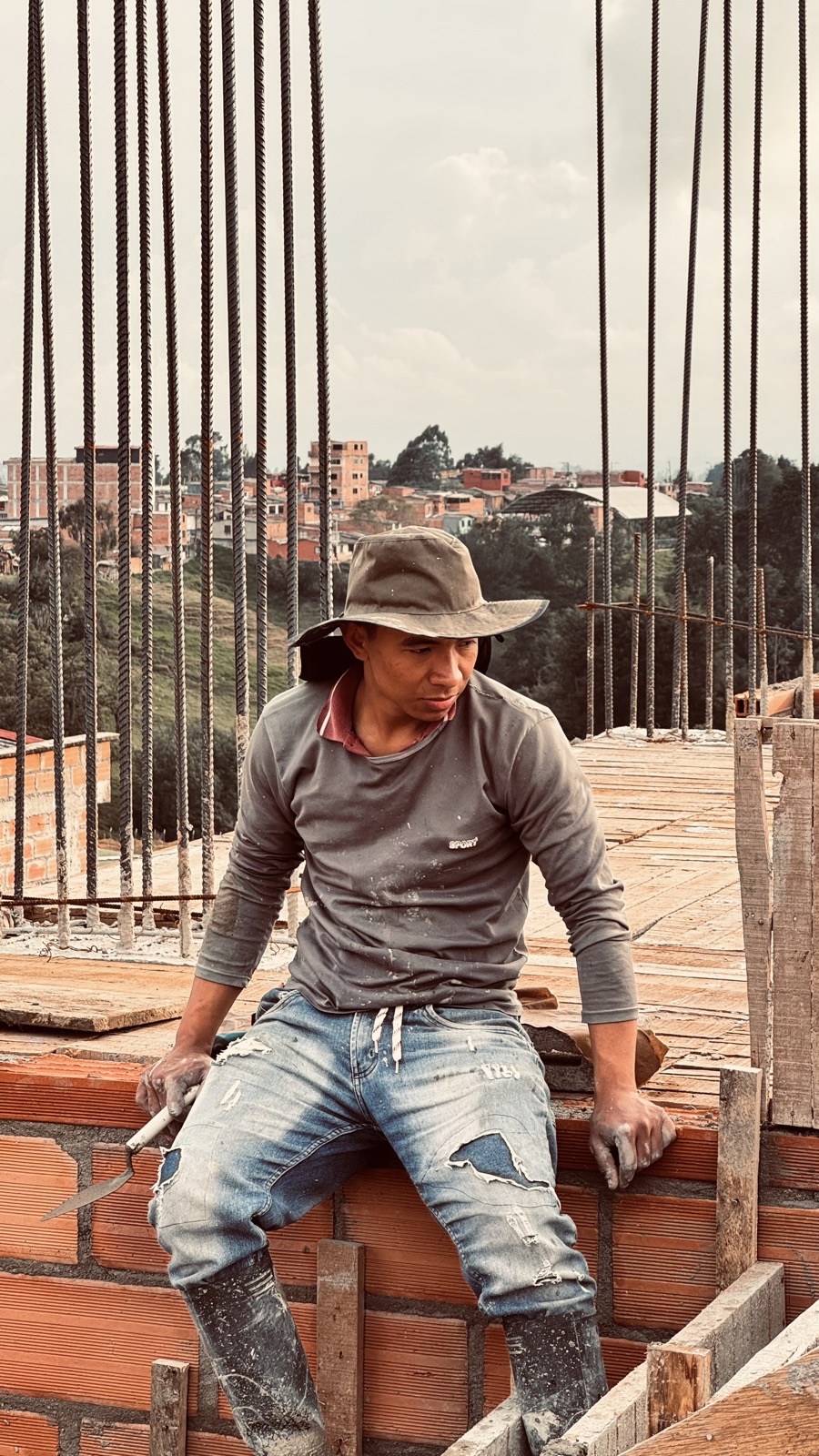 A worker rests among the rebar columns, the city of Medellín spreading behind.